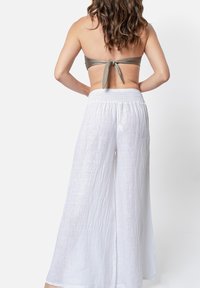 Pantaloni larghi bianchi in lino con una vita smock, abbinati a un top strapless verde oliva con dettaglio legato sulla schiena.