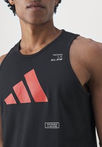 Černý bezrukávový top s červenými grafickými vzory, na přední straně s nápisem "ADIDAS" a textovými dodatky "TRAINING A49" a "IMPOSSIBLE IS NOTHING."