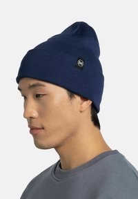 Gorro de punto azul marino con una parte superior puntiaguda y un parche de logo negro. Textura suave, ajuste ceñido y diseño acanalado.