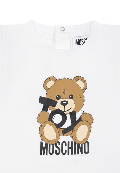 T-shirt in cotone bianco con una stampa di un orsetto cartone che tiene in mano la parola "TOY" in nero, con "MOSCHINO" stampato sotto. Maniche corte e colletto tondo.