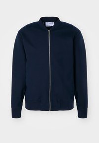 Veste bomber bleu marine avec fermeture éclair frontale et poignets et ourlet côtelés, présentée sur un fond uni.