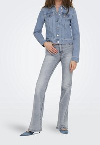 Vaaleansininen farkkutakki, jossa on hopeanväriset napit, kaksi rintataskua ja lyhennetty muoto. Yhdistetty vaaleansinisiin leveälahkeisiin farkkuihin ja samankaltaisiin kenkiin.