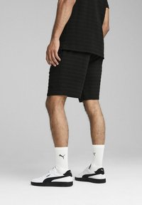 Shorts atletici negri cu un model texturat, asortați cu şosete albe și adidași negri și albi. Design simplu, minimalist.