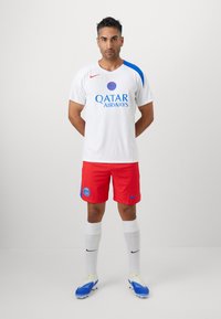 Hvid fodboldtrøje med blå detaljer og "QATAR AIRWAYS" logo; røde shorts med blå PSG emblem; hvide sokker; blå støvler.