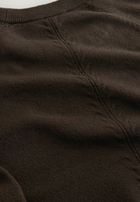 Pullover in maglia marrone con una superficie testurizzata, colletto a coste e cuciture visibili. Il tessuto appare morbido e leggermente peloso.