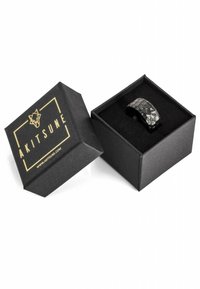 Texturierten schwarzen Ring in einer schwarzen Box mit weichem Innenteil; die Box hat ein goldenes Logo und besteht aus einem stabilen, matten Material.