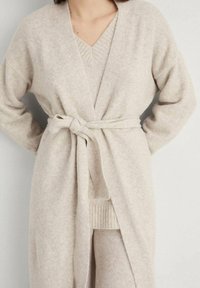 Cardigan in misto lana beige con cintura a cravatta, maglione a scollo a V sotto, polsini a coste e una finitura morbida e testurizzata.