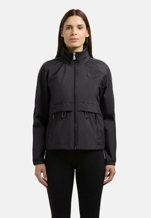 Vrouw die een zwart jack draagt met ritssluiting, hoge kraag, met rits afsluitbare zakken en koordjes in de taille, staand tegen een effen witte achtergrond.