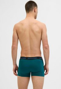 Tealfarbene Herren-Boxershorts mit einem schwarzen Bund, auf dem "JACK & JONES" in Blau steht. Glatte Stoffoberfläche mit taillierter Passform, von hinten betrachtet.
