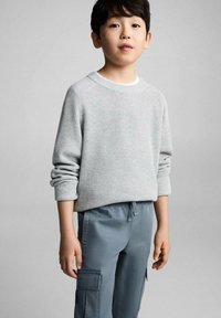 Šedý žebrovaný svetr s dlouhými rukávy a kulatým výstřihem, doplněný světle modrými cargo kalhotami s bočními kapsami a stahovací šňůrkou v pase.