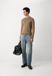 Bruine lange mouwen blouse, lichtblauwe relaxed-fit jeans, zwarte leren laarzen en een zwarte reistas. Katoenen materiaal met subtiele logodetails.