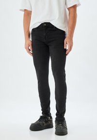 Jeans skinny negros de mezclilla, con una cintura de media altura, diseño de cinco bolsillos y detalles de costura sutiles. Combinados con zapatillas texturizadas.