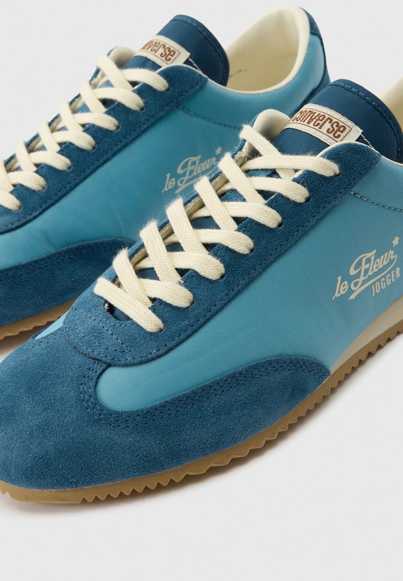 Blaue Wildleder- und Nylon-Sneaker mit cremefarbenen Schnürsenkeln, Gummisohlen und "le Fleur Jogger"-Markierung an der Seite.