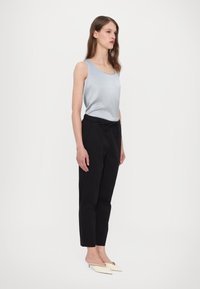 Light blue satin tank top, black tapered pants, and cream mules. The outfit features sleek lines with a soft texture and adjustable waistband.