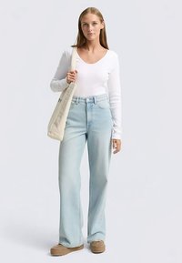 Witte top met lange mouwen en V-hals, lichtblauwe wijde spijkerbroek, en beige tas. Gestructureerde stof en lichtgewassen denim. Plateau sneakers.