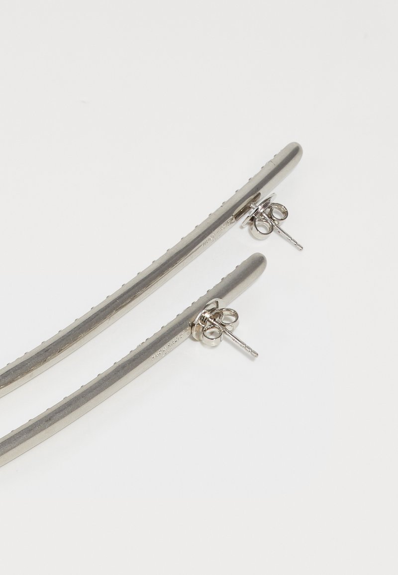 Silver-tone metal earrings with a sleek, elongated shape and textured surface, featuring butterfly backs for secure fastening.