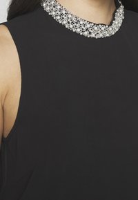 Top senza maniche nero con un colletto spesso, decorato con perle e accenti argento, realizzato in un tessuto liscio e elastico.