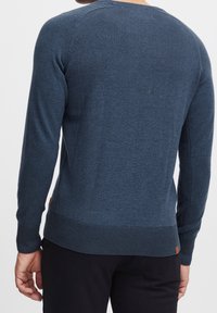 Maglione blu lavorato a maglia con maniche lunghe, collo rotondo, polsini e orlo a coste. Presenta un piccolo etichetta in pelle sul lato sinistro. Texture liscia.