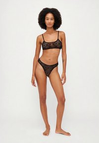 Fekete áttetsző fehérnemű szett, vékony pántos melltartóval és hozzáillő tanga bugyival. Virágminta díszíti az anyagot.