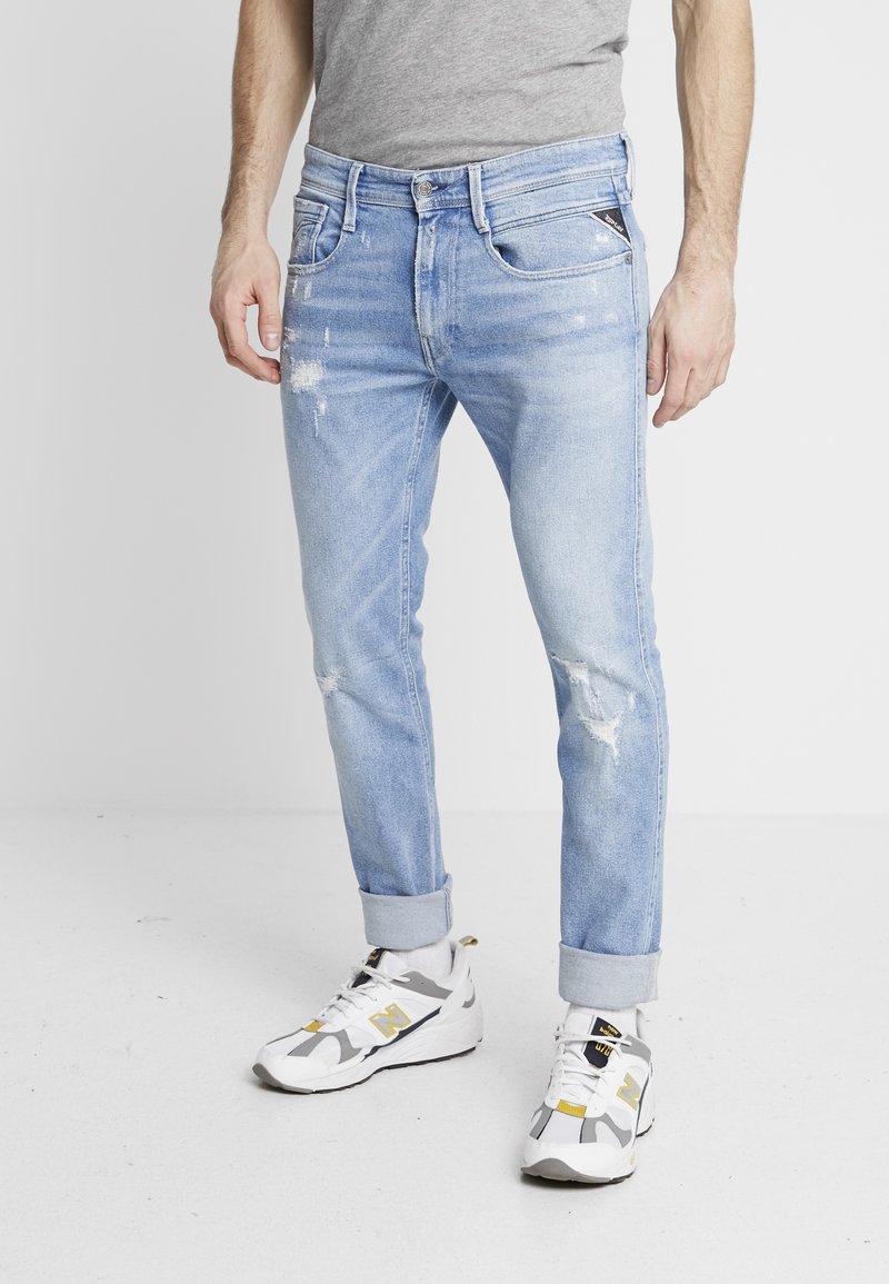 Ljusblå slitna jeans i slim fit, med uppvikta fållar, fickor och subtil blekning. Bärs med vita och grå sneakers.