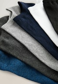 Pila de seis calcetines invisibles en azul marino, blanco, negro, gris claro, gris oscuro y azul, dispuestos superpuestos sobre una superficie blanca.