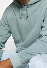 Ljusgrön hoodie i mjukt tyg med dragsko i huvan och ribbade muddar, kombinerad med ljusblå denim.