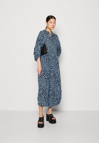Robe à motif zèbre bleu avec une coupe décontractée, des manches longues et un col rond. Associée à des sandales à plateforme épaisses noires. Accent avec un sac à main noir.