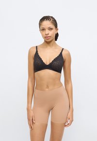 Μαύρο δαντελένιο bralette με σχέδιο από κυματιστό άκρο, συνδυασμένο με καλσόν σε γυμνού χρώμα χωρίς ραφές. Και τα δύο εφαρμόζουν στενά στο σώμα, αναδεικνύοντας την υφή και το σχήμα.