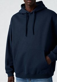 Námornícka modrá mikina s kapucňou má kengurské vrecko, šnúrky na stiahnutie, rebrované manžety a voľný strih. Vyrobená z mäkkej zmesi bavlny.