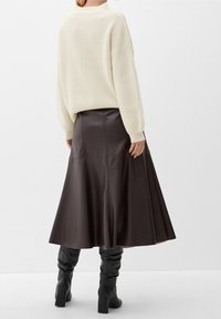 Suéter de canalé crema con hombros caídos, combinado con una falda de cuero marrón oscuro en forma de A y botas altas negras con tacones cuadrados.