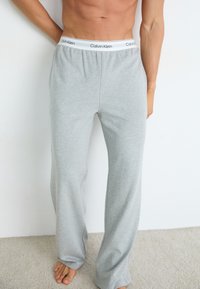 Graue Baumwoll-Loungewear-Hosen mit lockerer Passform, ausgestattet mit einem elastischen Bund mit schwarz-weißer "Calvin Klein"-Markenbezeichnung. Weiche Textur.