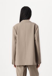 Beige skreddersydd blazer med en strukturert silhuett, spisse revers og lange ermer. Glatt stoff og rene linjer definerer designet.