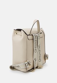 Beige texturerad läderryggsäck med svarta detaljer, som har guldfärgade metalldelar och justerbart band präglat med "Valentino." Rektangulär form.