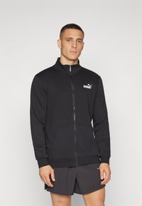 Black zip-up jacket made of textured fabric with a high collar, featuring two front pockets and a white Puma logo on the left chest.