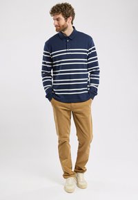 Polo à manches longues à rayures marines et blanches, avec patte de boutonnage à deux boutons, associé à un pantalon beige et des baskets crème. Texture de tissu lisse.