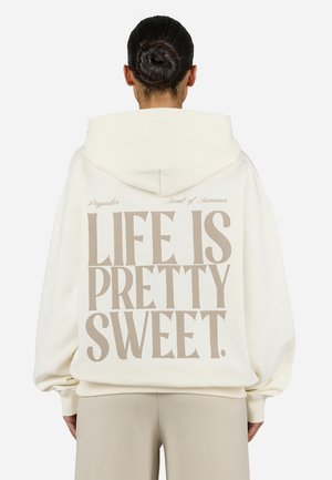 Cream hoodie with oversized fit, featuring a large beige print saying "LIFE IS PRETTY SWEET" on the back. Drawstring hood and ribbed cuffs.