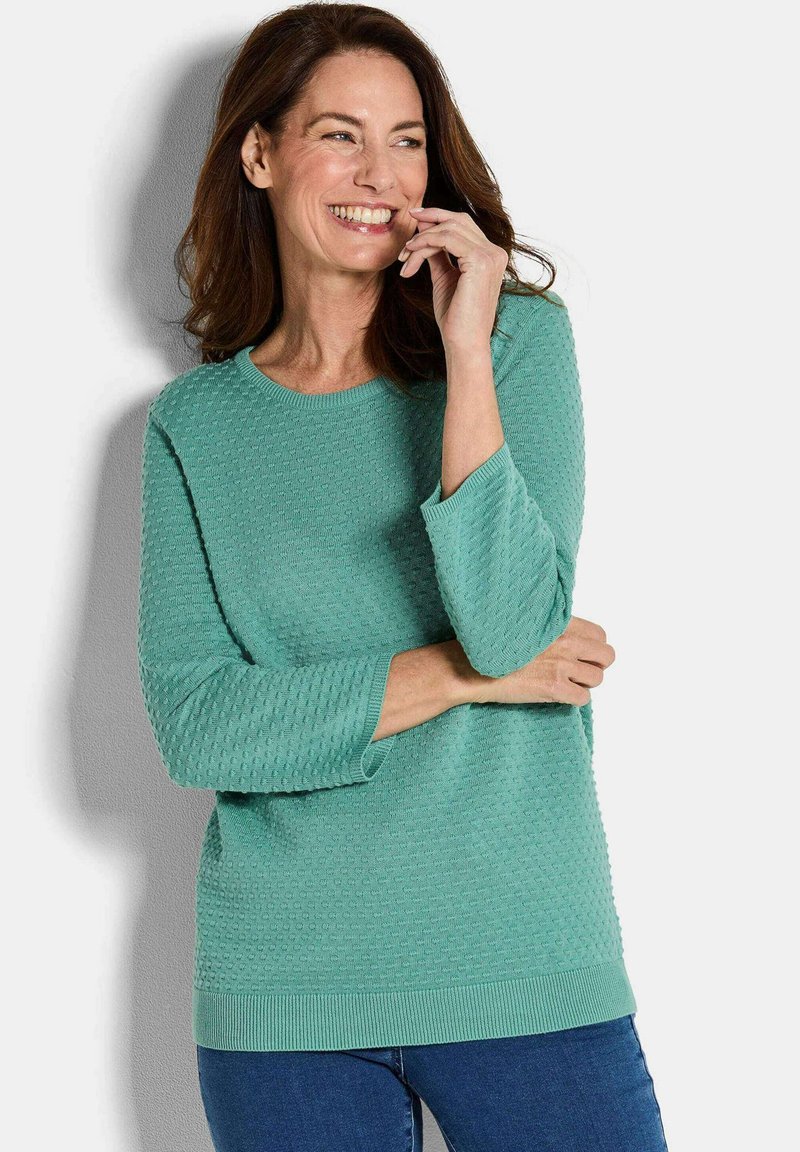Helles türkisfarbenes Sweatshirt mit strukturiertem Muster, rundem Ausschnitt, 3/4-Ärmeln und geripptem Saum. Kombiniert mit blauen Jeans hat das Gesamtoutfit einen lässigen Sitz.