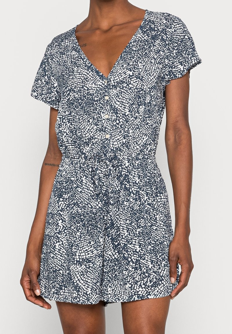 Short-sleeve romper made of navy fabric with a white abstract pattern, featuring a V-neckline and button closure at the front.