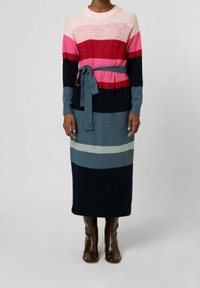 Stickad randig klänning med rosa, röd, blå och marinblå band, med midjeband och långa ärmar, kompletterad med bruna knähöga stövlar.