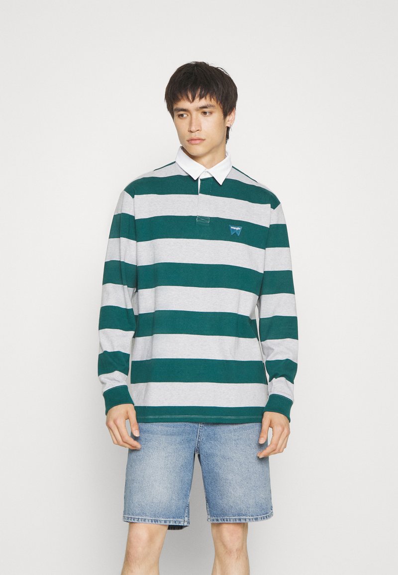 Poloshirt met lange mouwen in groen en grijs horizontale strepen, met een kraag en een klein logo op de linkerborst, gecombineerd met denim shorts.