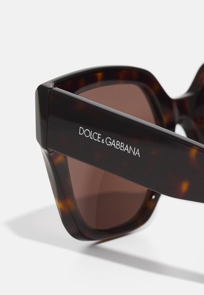 Solsystem i sköldpaddsmönster med bruna linser, med geometrisk form och en svart stav prydd med "DOLCE & GABBANA." Slät textur.