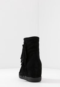 Černé semišové kotníkové boty s designem se třásněmi na vnější straně, zaoblenou špičkou a plochou gumovou podrážkou.