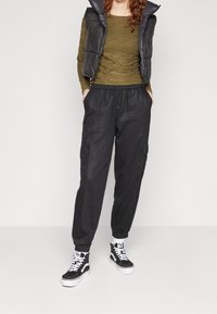 Pantaloni cargo grigio scuro con vita elastica, due tasche laterali e polsini affusolati, abbinati a una maglietta aderente verde oliva e sneakers nere.