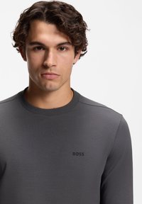 Graues Langarmshirt aus glattem Stoff mit rundem Ausschnitt und dezentem "BOSS"-Logo in Schwarz auf der Brust.