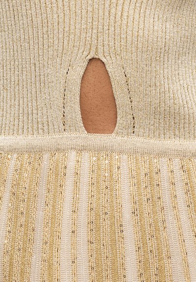 Gebreide beige stof met verticale paillettenstrepen en een druppelvormige uitsparing die de huid eronder onthult.