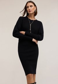Vestito a maglia nero fino al ginocchio realizzato in morbido tessuto. Presenta maniche lunghe e una silhouette aderente, con scollatura tonda.