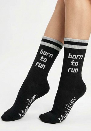 Czarne bawełniane skarpety z białym napisem "born to run" z przodu oraz napisem "Marilyn" w stylu pisma na boku, z dwoma szarymi paskami na górze.