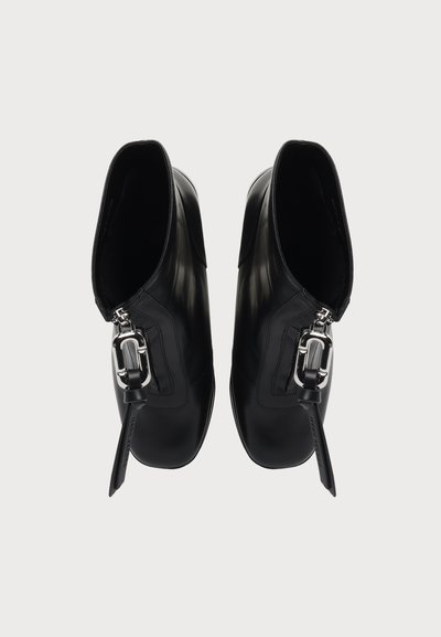 Paire de bottines noires en cuir avec des boucles latérales argentées et des brides en cuir, vues de dessus sur un fond clair.