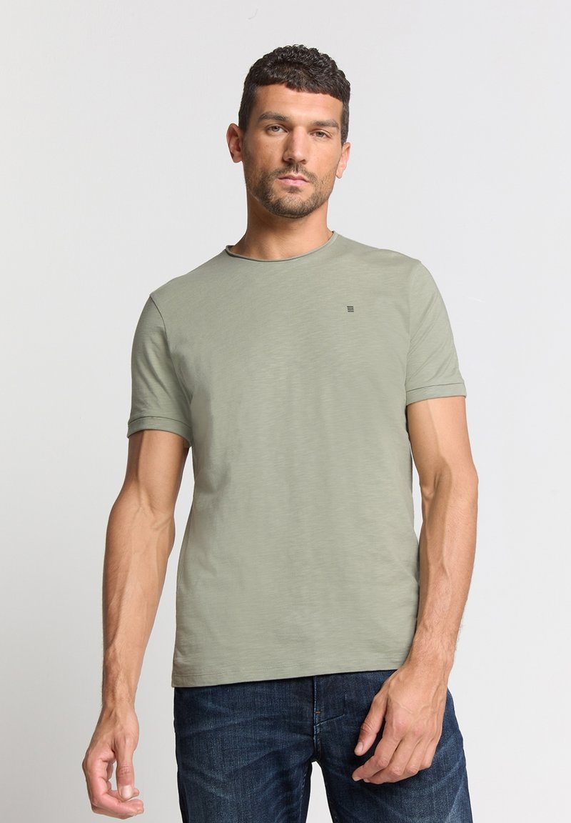 Lichtgroene t-shirt met korte mouwen en ronde hals, met een subtiele logo op de borst, gecombineerd met donkerblauwe denim jeans. Zachte textuur, casual fit.