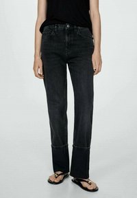 Jeans de mezclilla negros con corte recto, presentando un dobladillo deshilachado y detalles de costura sutiles. Combinados con sandalias negras.